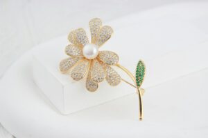 Close-up of a luxurious flower-shaped gold brooch adorned with jewels and a pearl centerpiece on a white background.