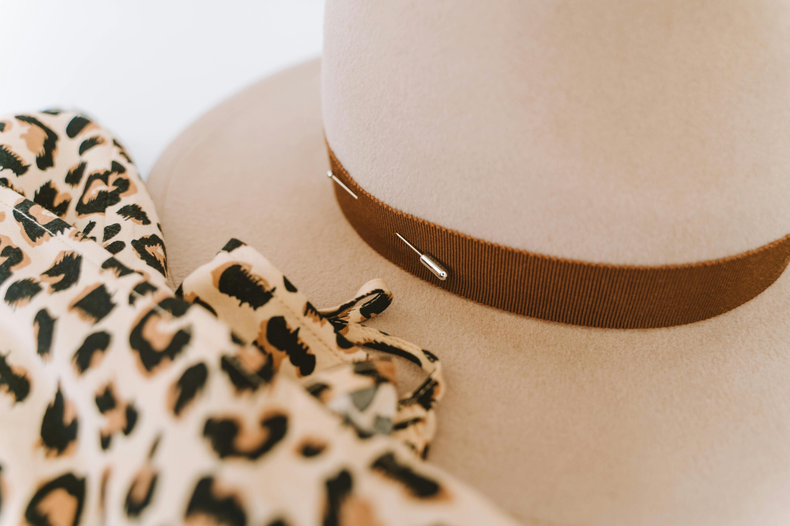 Close-up of a stylish beige hat adorned with a leopard print scarf and a safety pin accent.